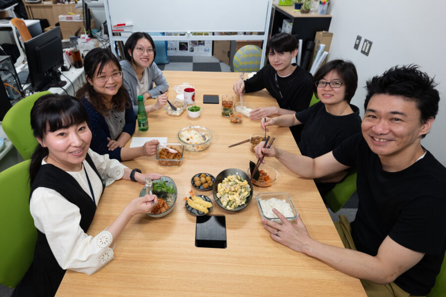 萩原チームリーダーと、5人のチームメンバーが、各国料理のお弁当を広げている